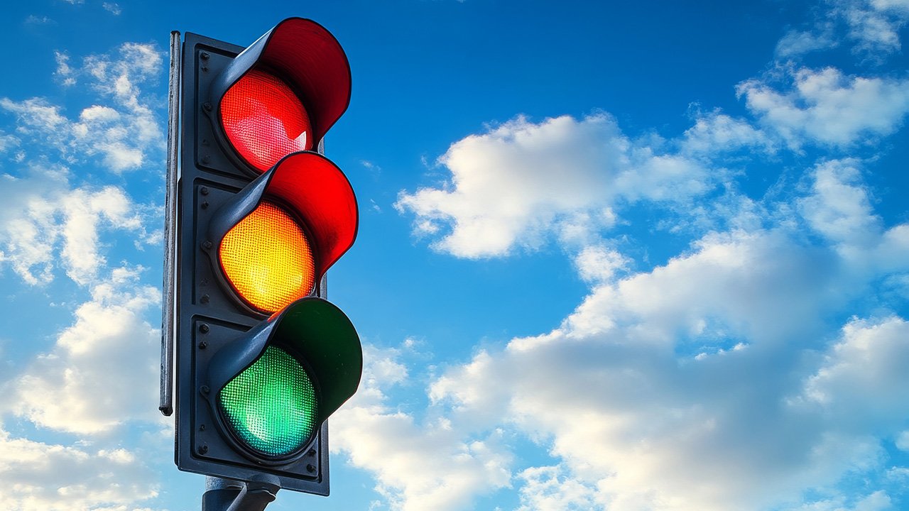 A traffic signal with red, yellow, and green lights against a blue sky with clouds