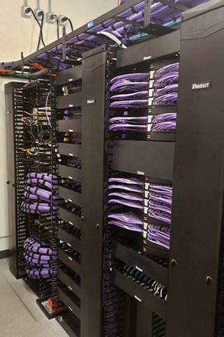 Black Panduit racks and cable managers built out with purple category 6a cabling, patch cords, patch panels, and jacks, in a telecommunications room