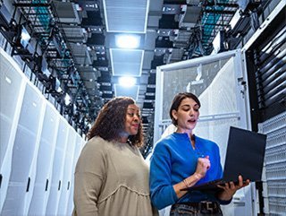 2 women look at a laptop computer in front of a bank of data center cabinets