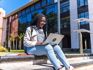 a university student works on a laptop computer outside on a campus
