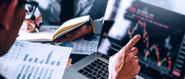 A person points to financial charts on a laptop screen during a business meeting.