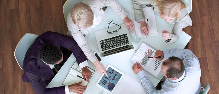 Overhead view of four business professionals collaborating around a table with charts and a laptop.