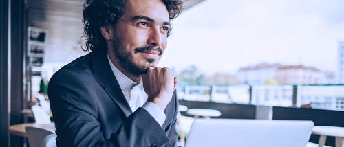 A businessman in a suit looking thoughtful while sitting with a laptop.