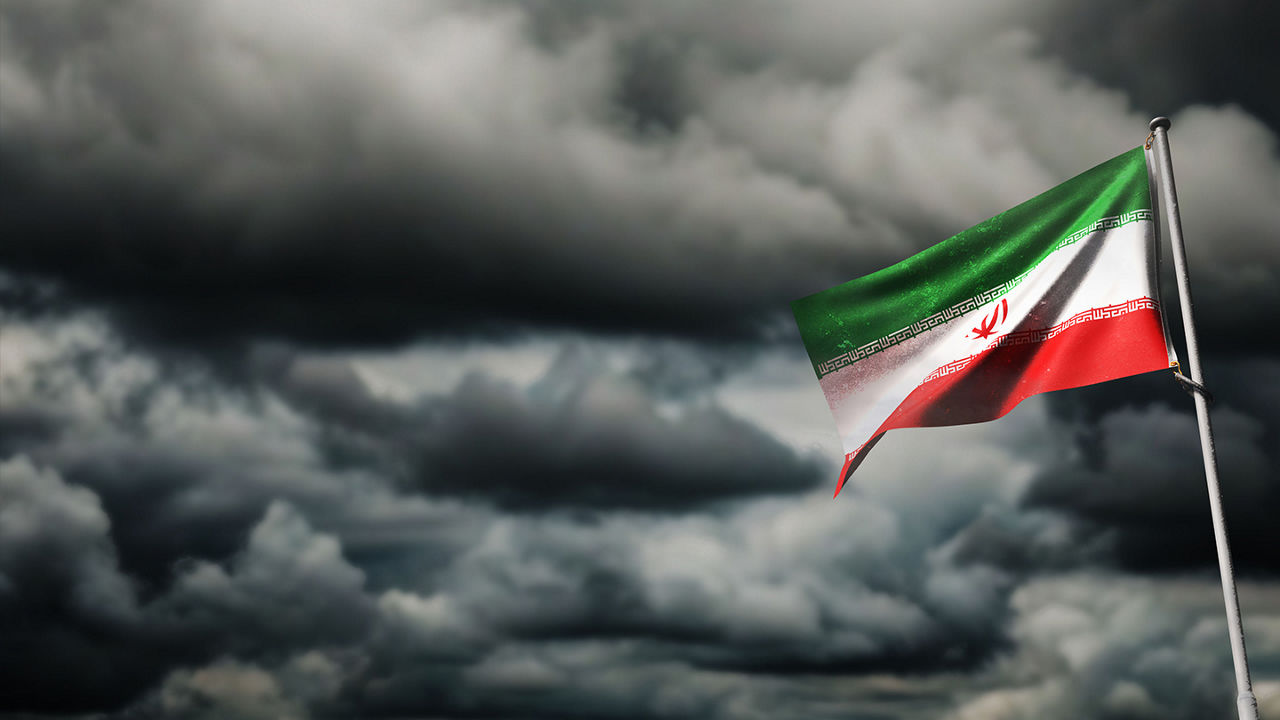 Iranian flag waving with dark, cloudy background.
