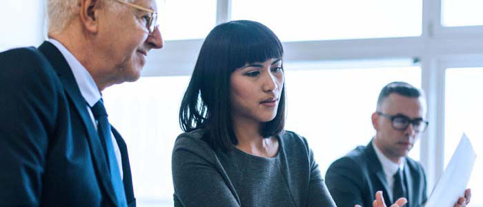 Three business professionals in an office setting reviewing documents.