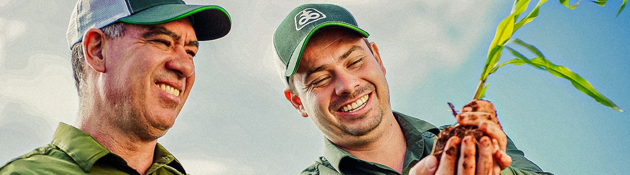 Dois homens com camisas e bonés da Pioneer analisando uma muda de milho.