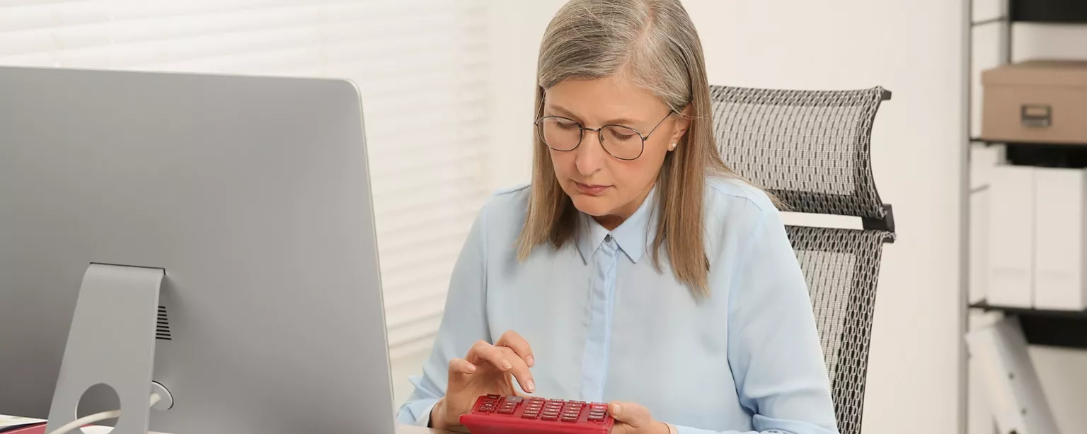 A senior accountant inputs numbers on her calculator while working at a desk.