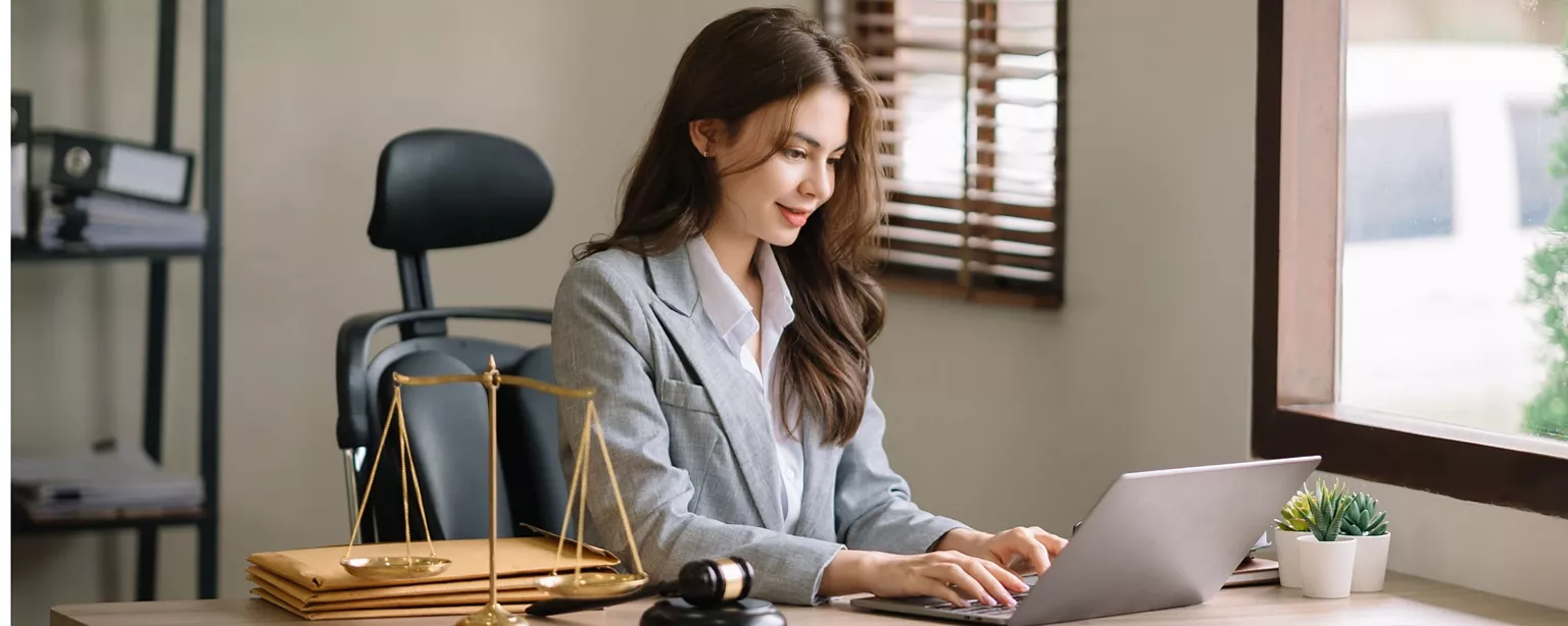 A lawyer works at her desk, next to decorative scales of justice and gavel.