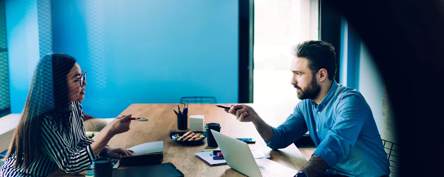 An interview for a technology job is underway in a modern office; a woman and a man are engaged in conversation.