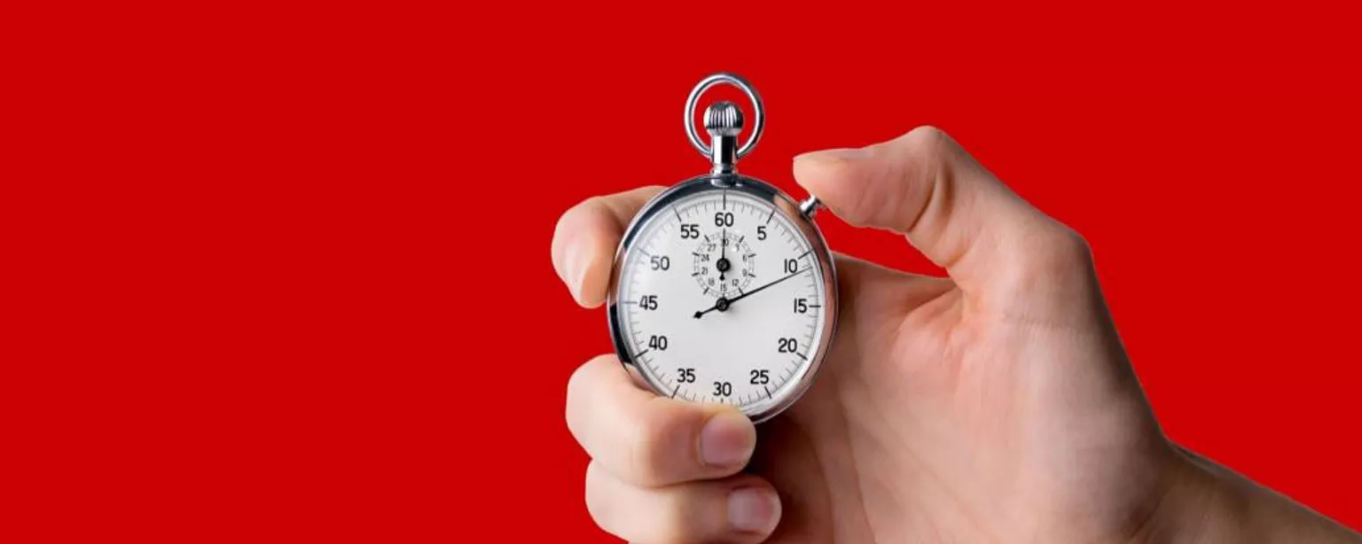 A person's hand holding a silver stopwatch against a red background.