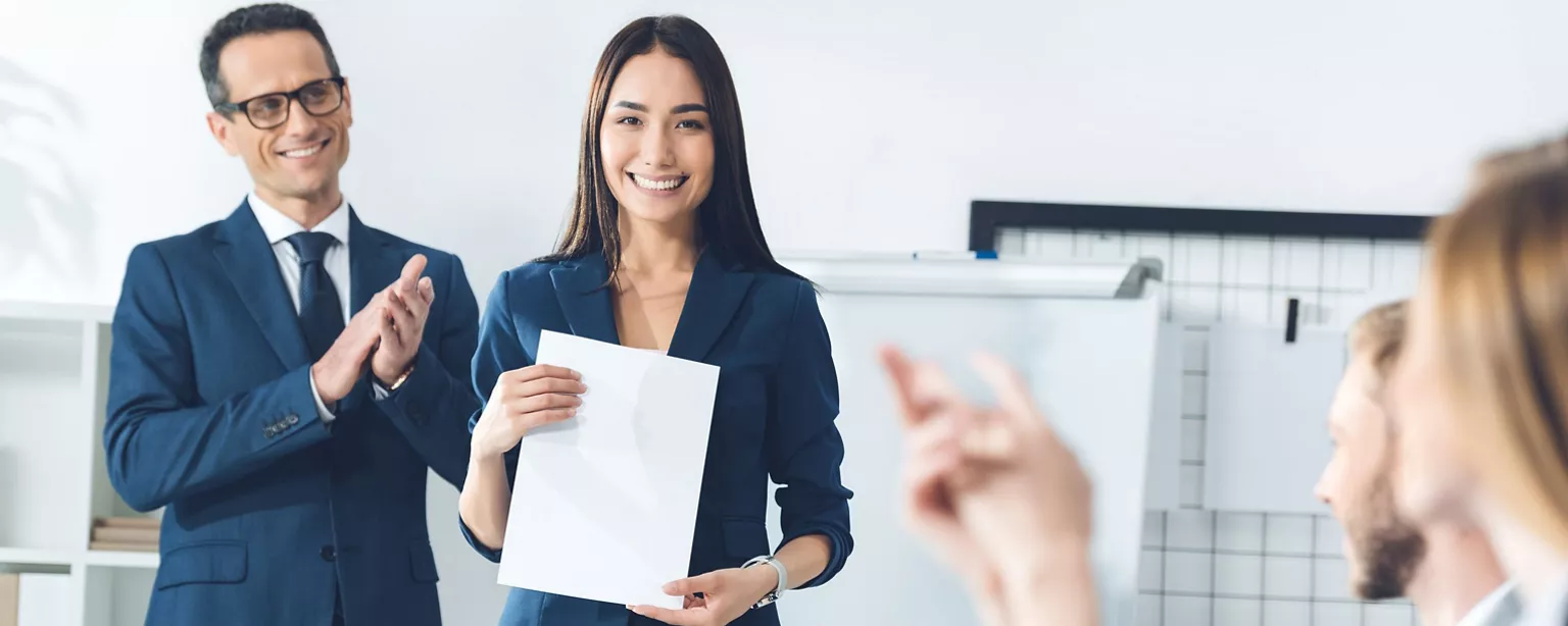 A lady standing at the front with information and three colleagues applauding her