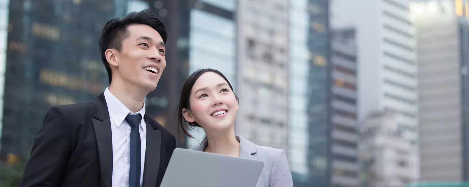 A man and a woman standing outside an office building together looking into the distance