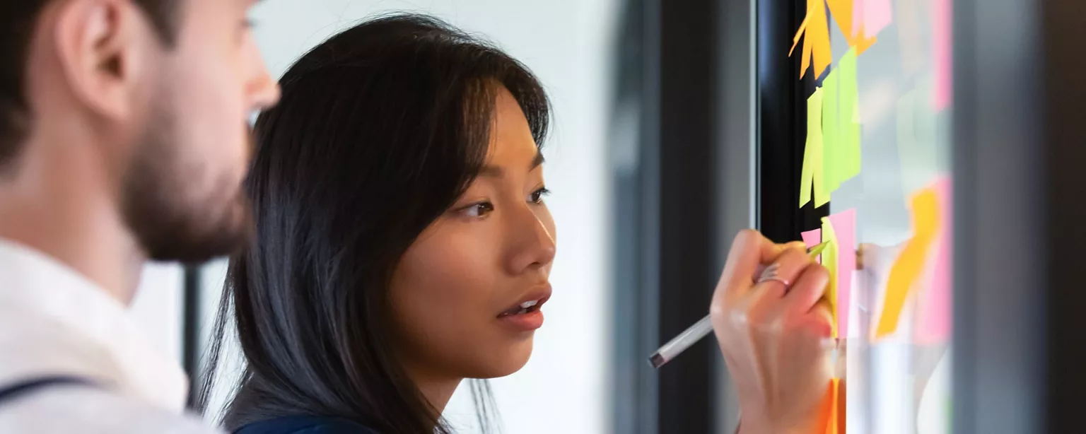 A businessman and a businesswoman scribbling on the wall of a writing pad to discuss a problem