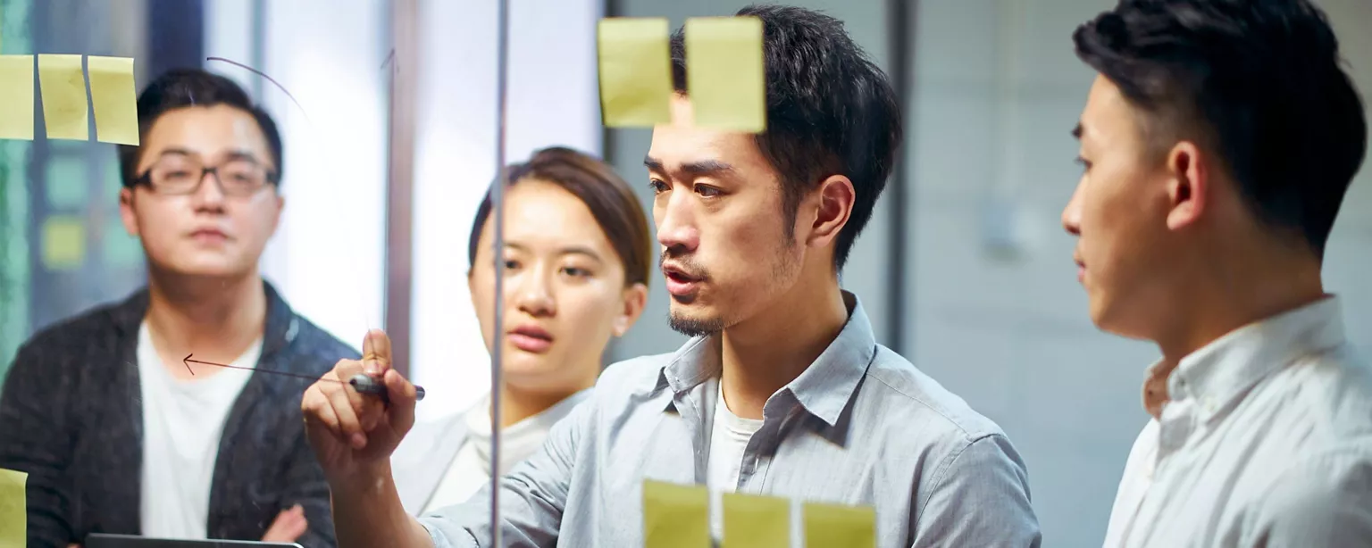 Three male tech professionals and one female tech professional discussing an issue in front of a transparent whiteboard 