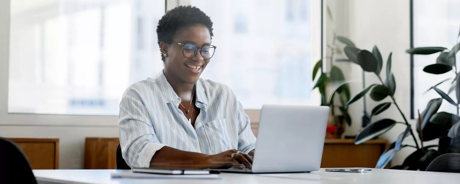 A woman absorbed in her work to earn an IT certification smiles as she works at a laptop.