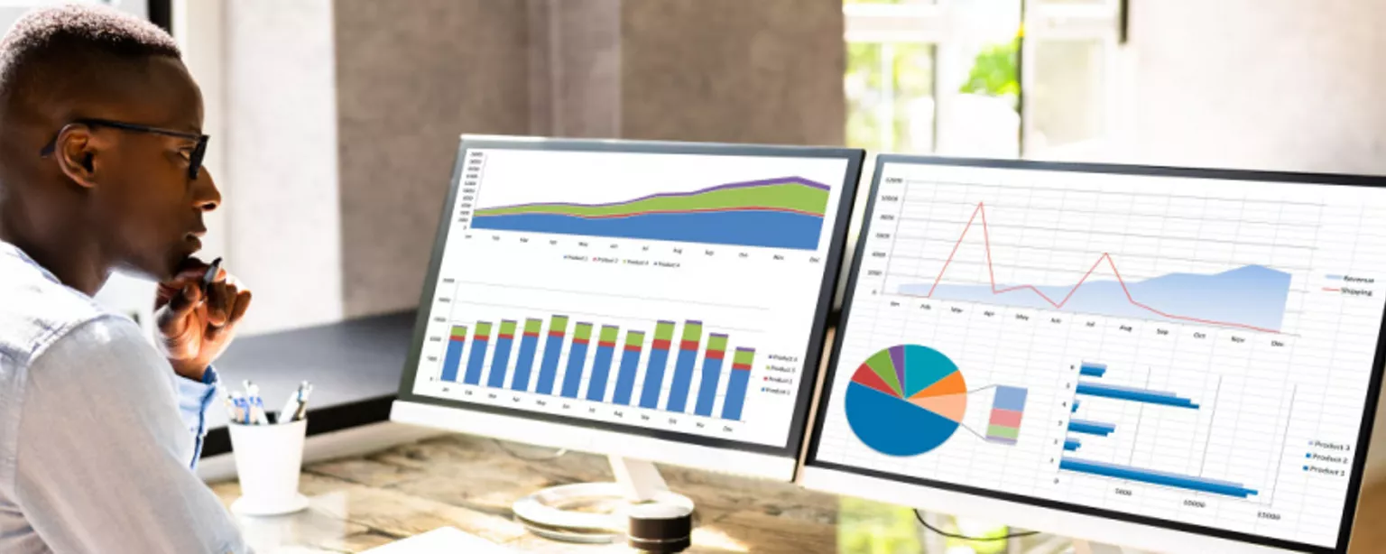 A man with glasses, a financial analyst, looking at financial charts on two computer screens.