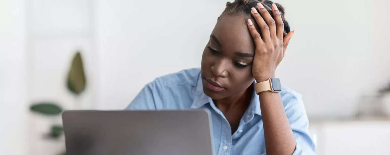 Woman sitting at a desk, head in hand, looking glum and starting at her laptop screen.