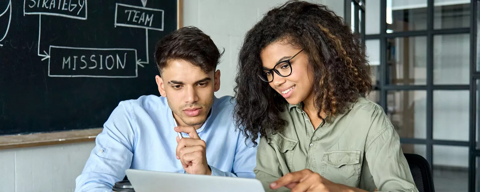 A female mentor explains a concept to a male mentee in a workplace environment.