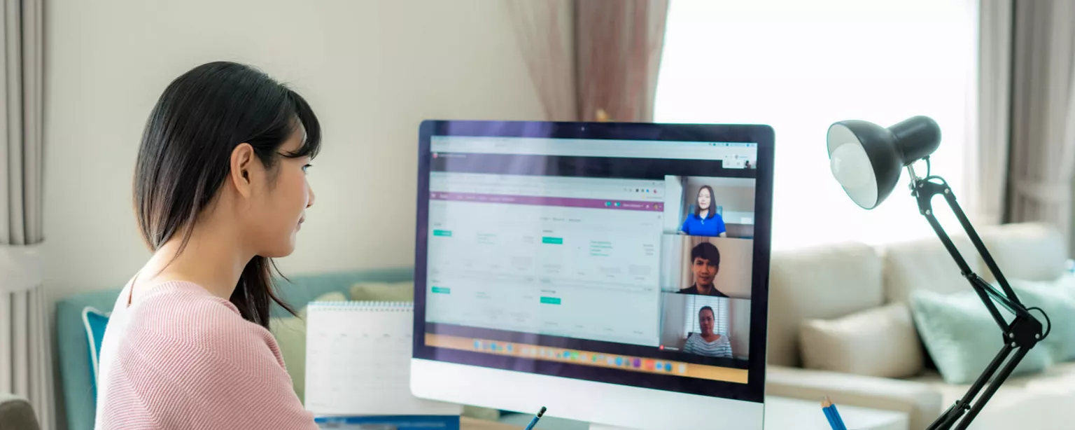 A young woman in a pink sweater sitting in front of a computer, engaging in virtual learning.