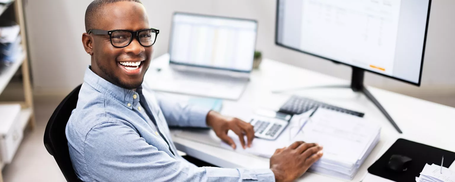 A young general accountant, or staff accountant, uses a calculator as he works at his desk.