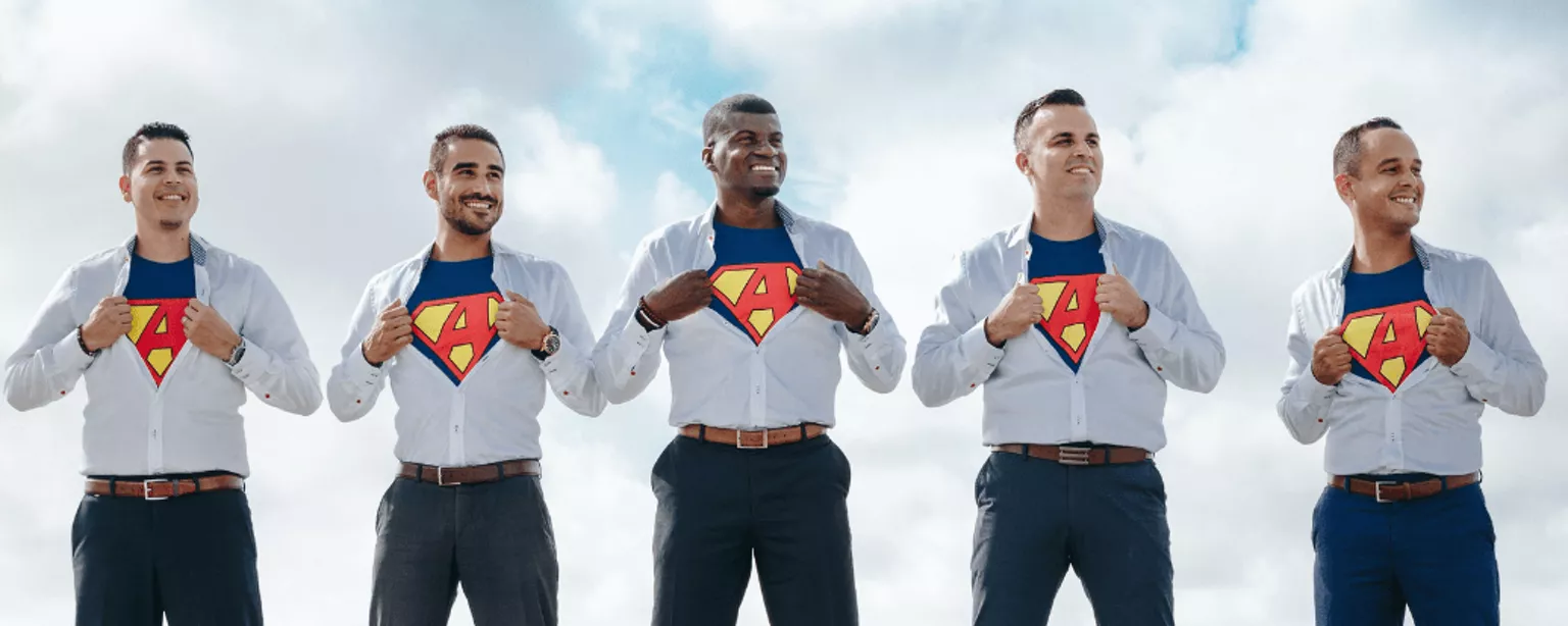 5 Männer reißen ihre weißen Business-Hemden auf; darunter tragen sie T-Shirts mit einer Superman-Aufschrift.