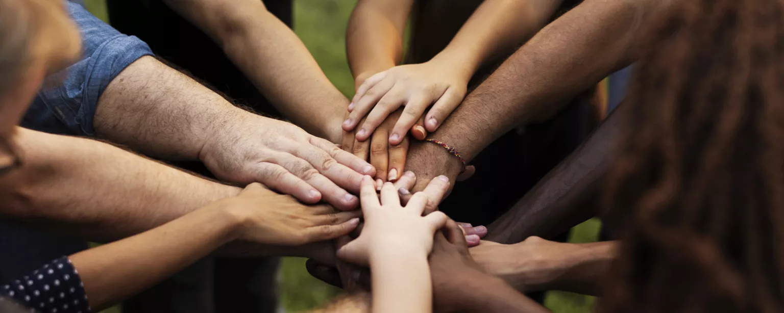 Group of diverse volunteers putting hands together in circle to show teamwork.