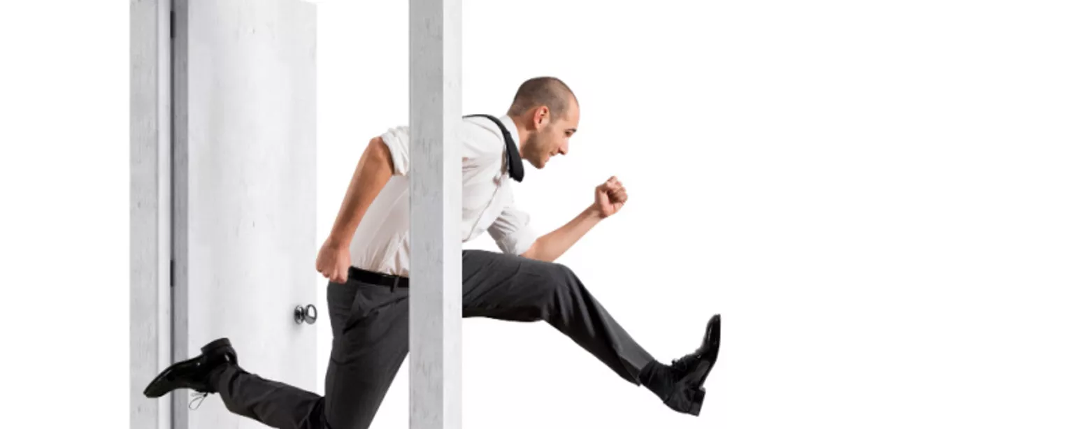 A man in a white shirt and black pants jumps through an open doorway.