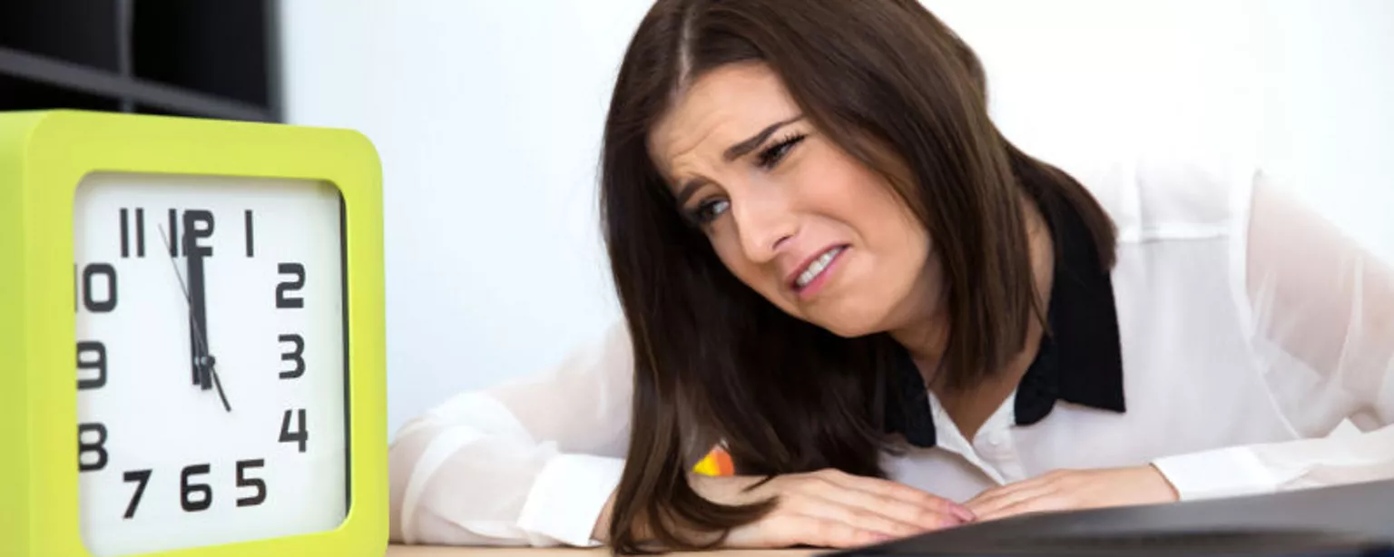 A woman stares at a clock with hands at 12 o'clock as she waits for time to pass at her job.