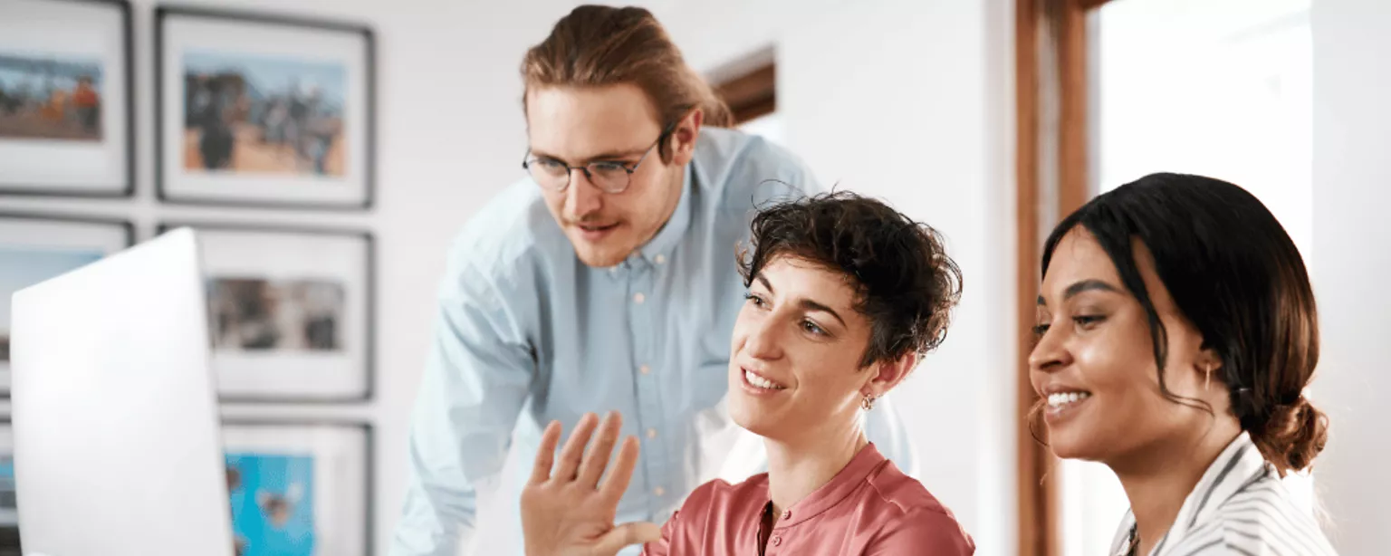 Two women and a man sitting around a computer in an office