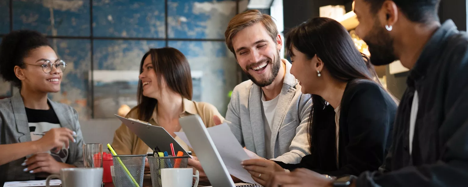 A group of colleagues smile while collaborating during a team meeting in a conference room.