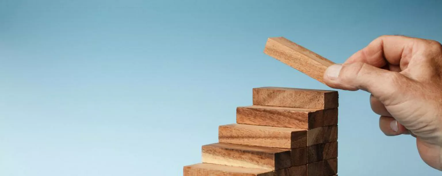 Wooden blocks arranged as steps, with a hand placing a block at the top step.
