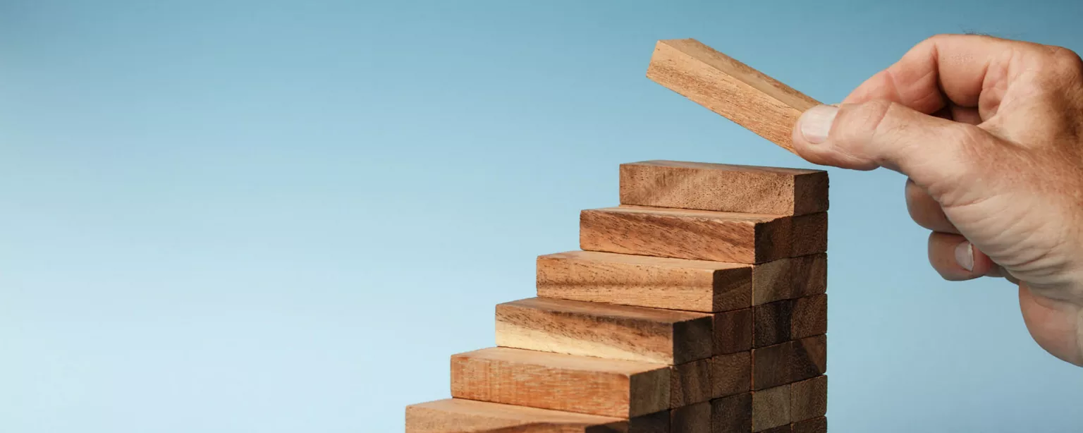 Wooden blocks are arranged as steps, with a hand placing a block at the top step.