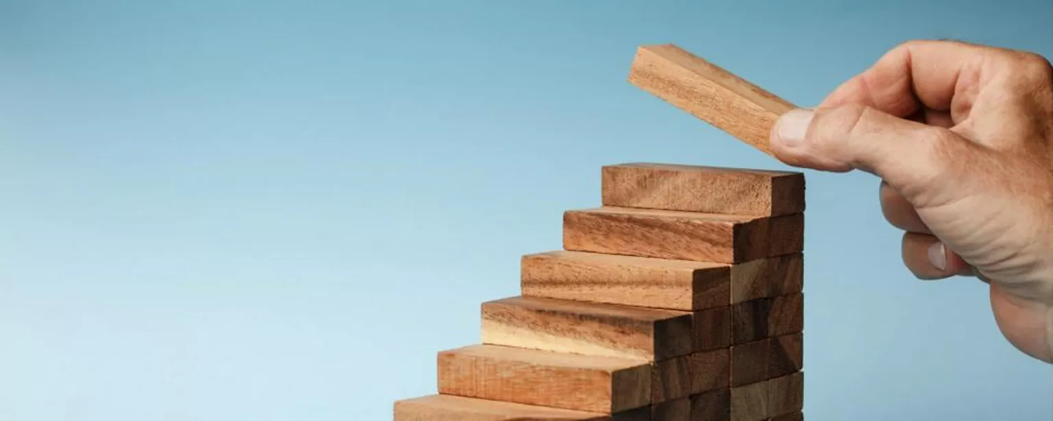 Wooden blocks arranged as steps, with a hand placing a block at the top step.