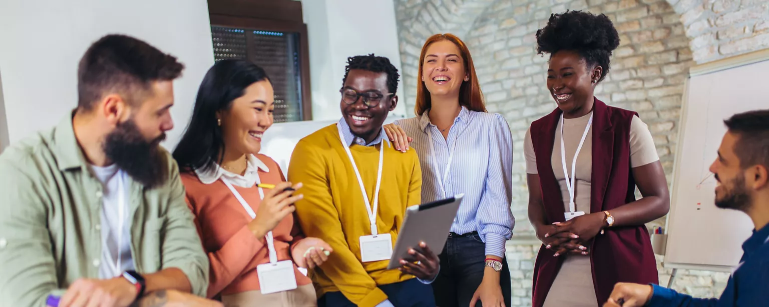 A group of colleagues gathers together, smiling and collaborating during a team meeting in an office.