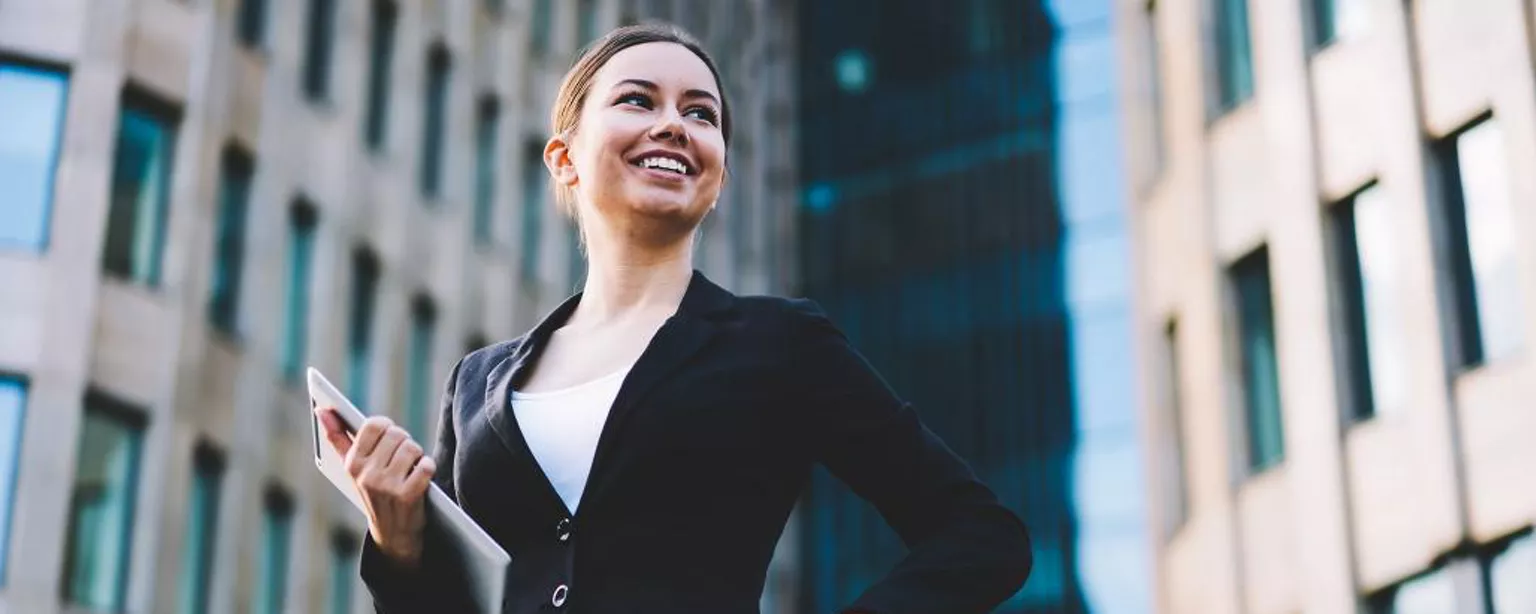 Une femme professionnelle souriante, tenant des documents, entourée de gratte-ciels.