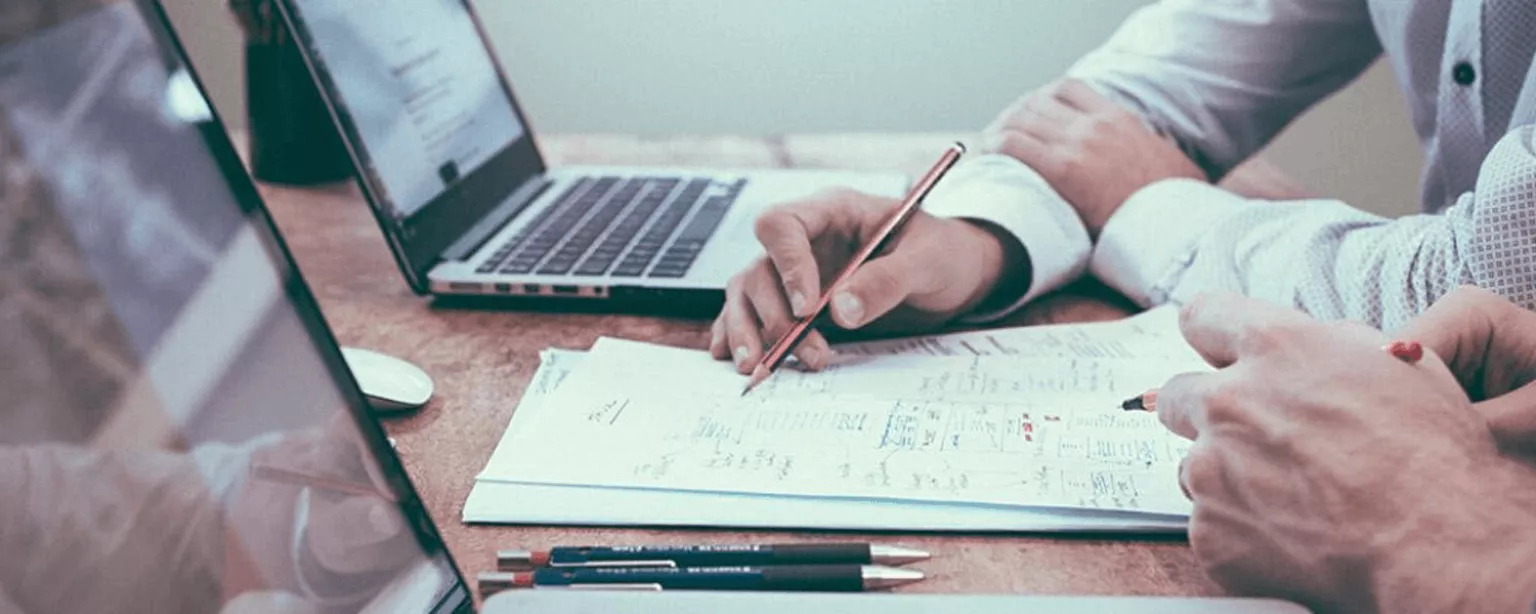 Zwei Männer mit Notebook gehen gemeinsam Unterlagen durch.