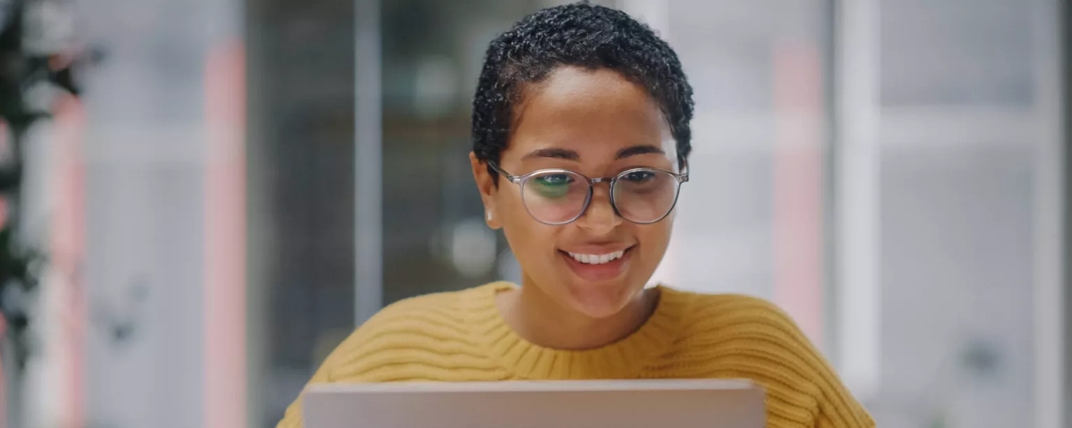 Why It's a Great Time to Be an Administrative Assistant — smiling woman in yellow sweater in front of laptop