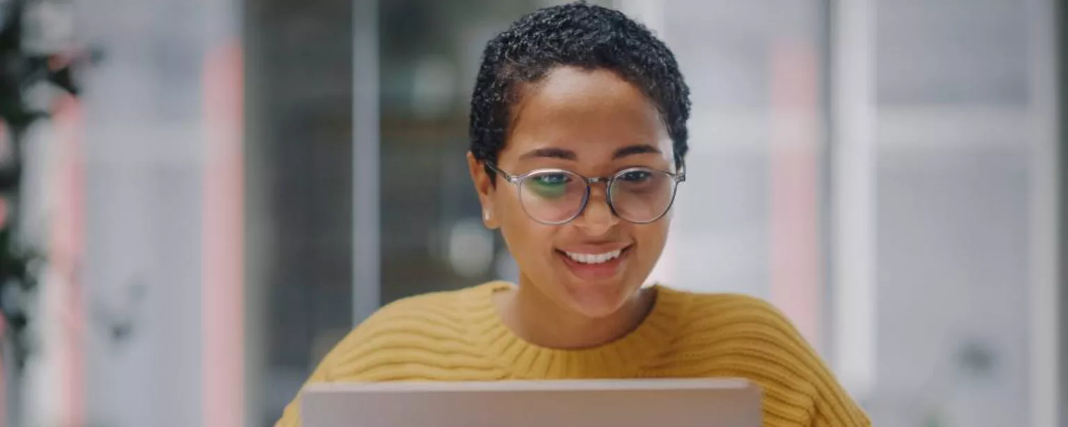 Why It's a Great Time to Be an Administrative Assistant — smiling woman in yellow sweater in front of laptop