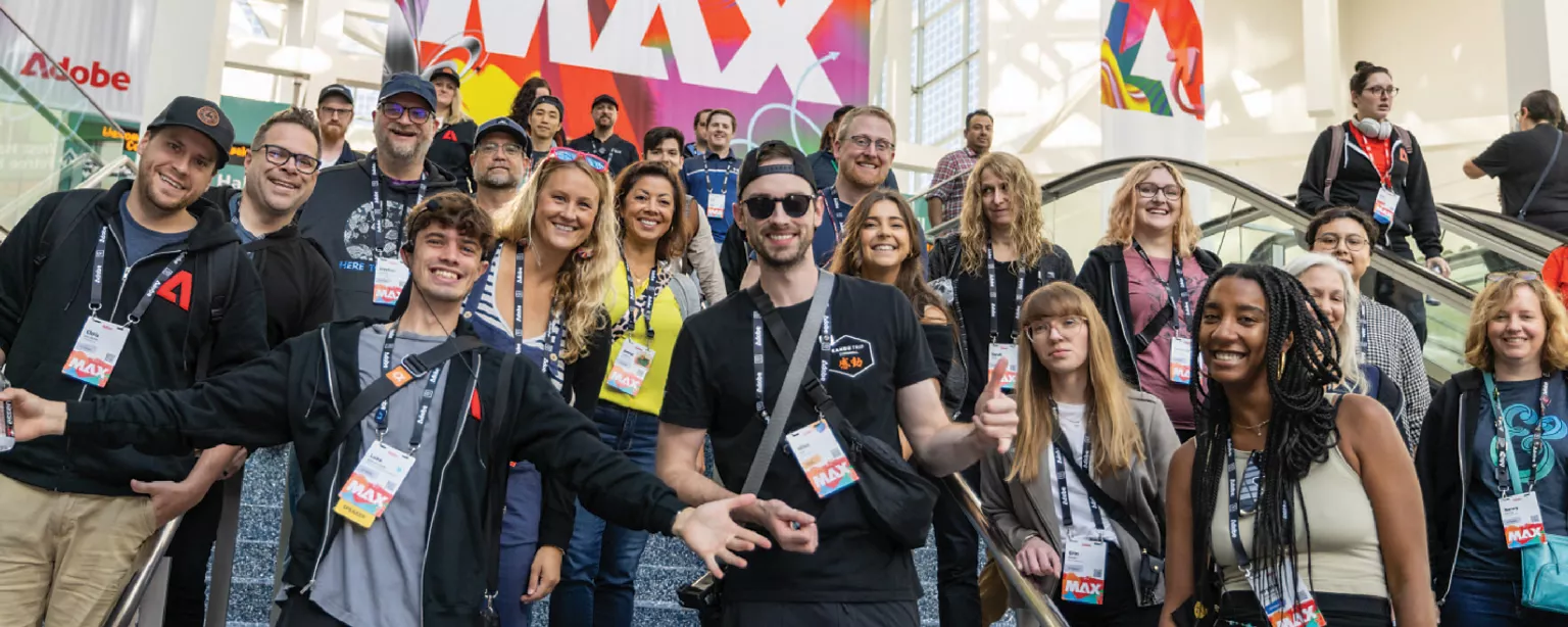 Adobe Max conference attendees smiling with MAX banner behind them.