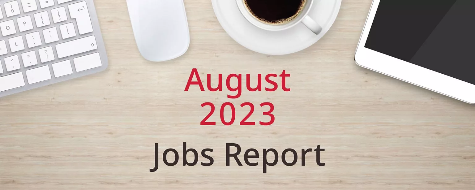 On a wooden desktop, positioned below a keyboard, mouse, cup of coffee and a tablet computer, are the words, “August 2023 Jobs Report.”