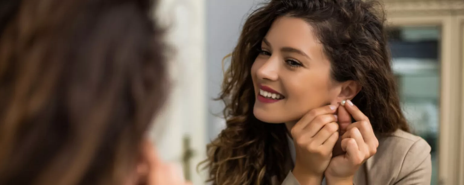 Back-to-office attire: 4 tips to help you dress for a more flexible workplace - photo of smiling woman in business blazer putting on earring in mirror