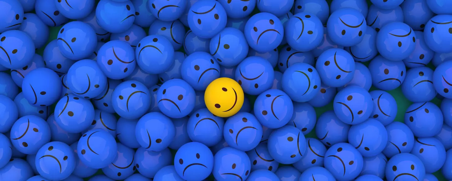 A yellow ball with a smiley face in a sea of blue balls with frowning faces.