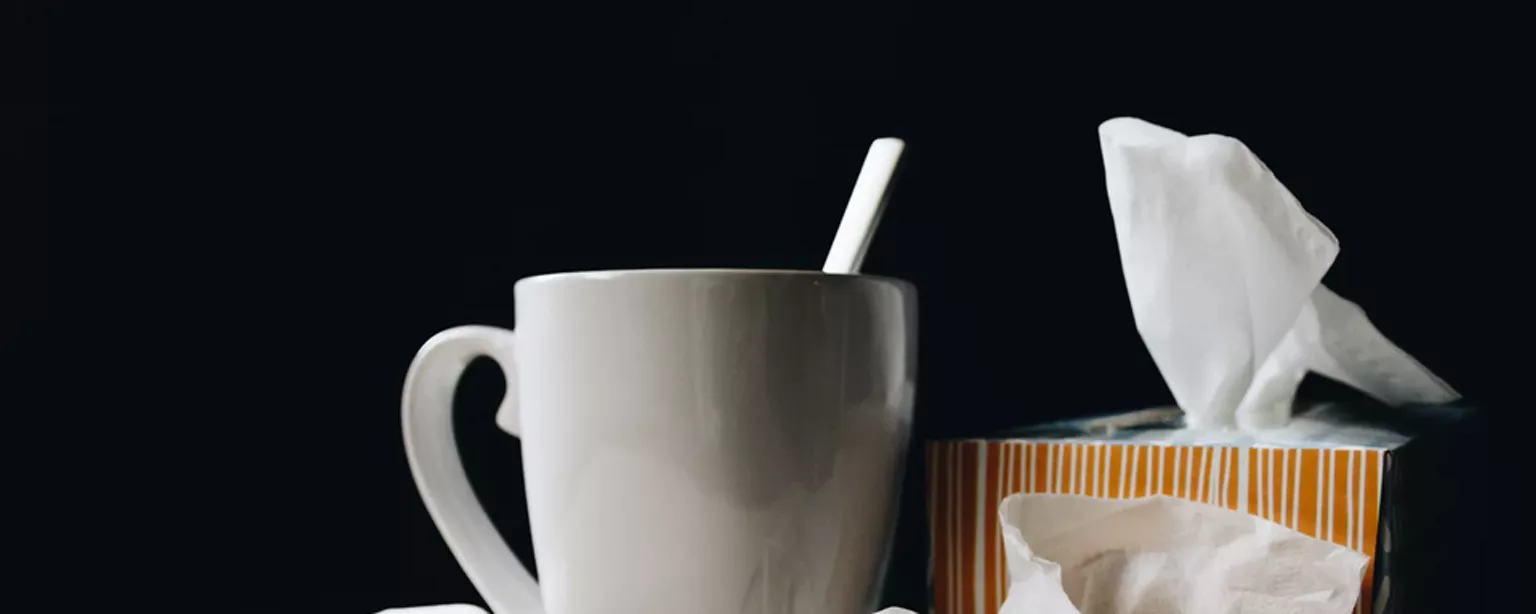  Arrangement aus Teetasse, Taschentücher-Box, benutzten Papiertaschentüchern und abgelegter Brille.