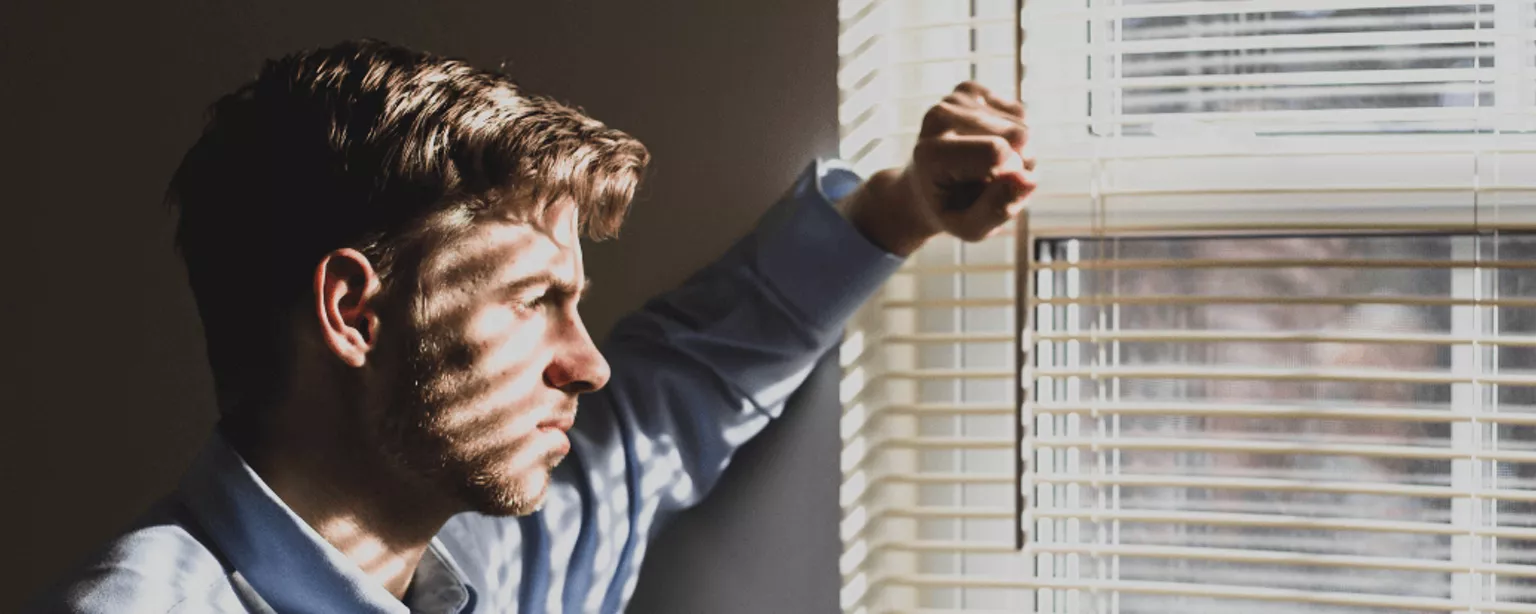 Mann im Business-Hemd starrt bedrückt aus einem Fenster