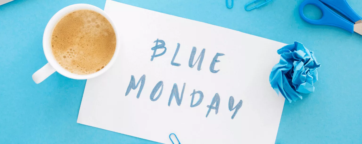 Schreibtisch in blau mit Kaffeetasse und Blatt mit Aufschrift Blue Monday