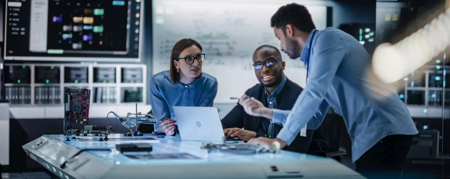 Three members of a technology team working in a lab and discussing a technical problem.