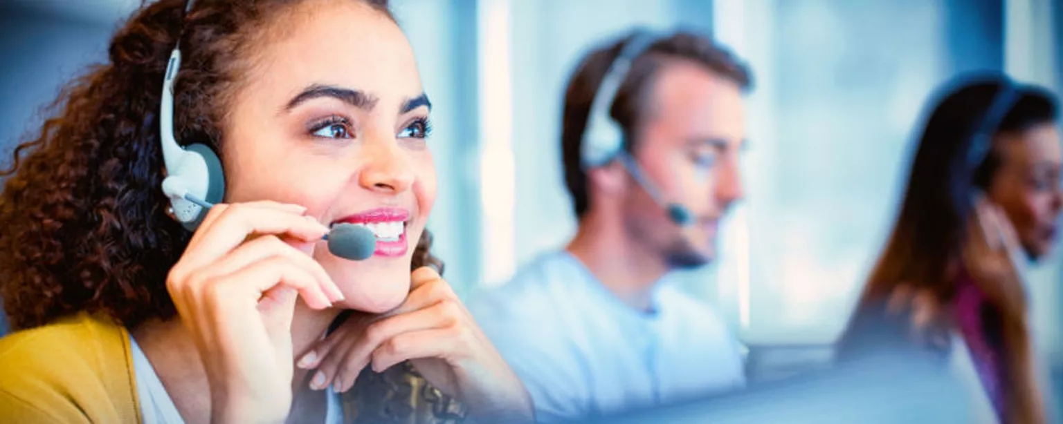 A smiling woman and two customer service coworkers wear headsets as they handle on-the-job tasks.