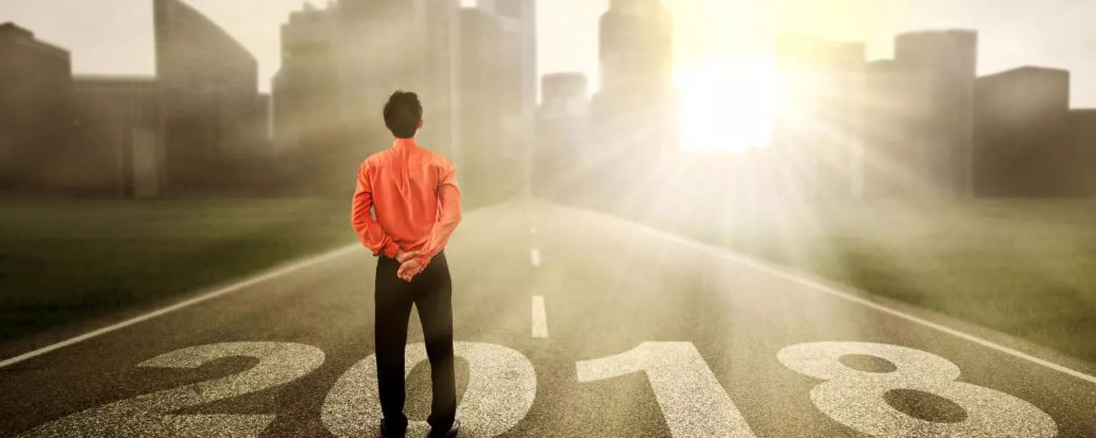 Man standing on a road marked 2018, looking at a city and, perhaps, a job promotion
