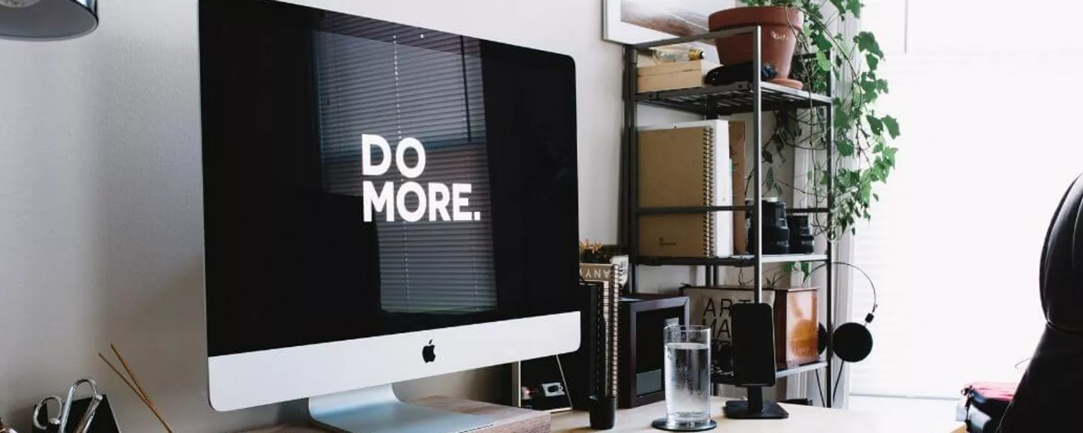 Auf einem Schreibtisch steht ein Computer, dessen Bildschirm die Worte „Do more” zeigt