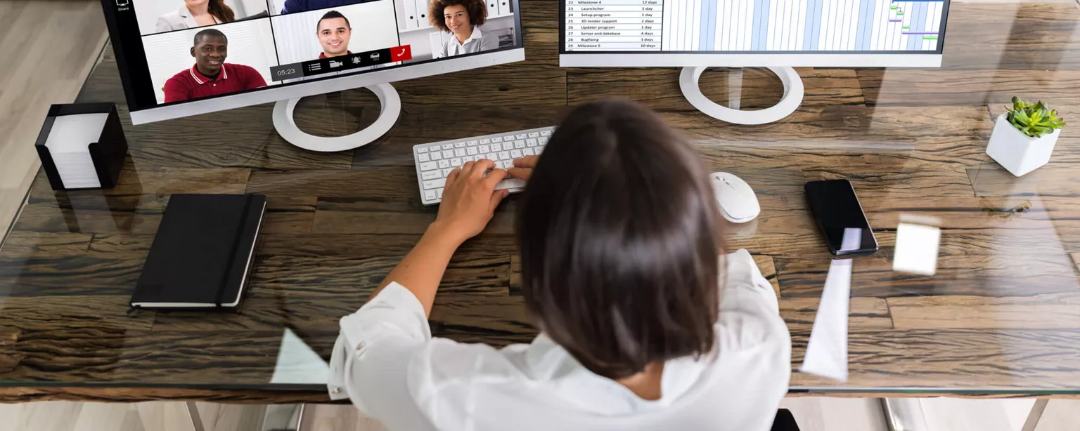 Why Your Company Needs a Chief Remote Work Officer — person working at desk with two desktop screens, one with faces on a video call